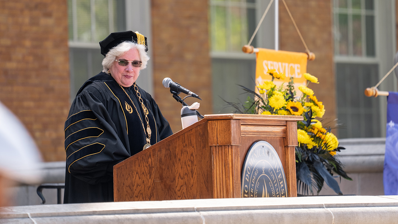 President Connie Gallaher stands at a podium on the front steps of Erskine to welcome everyone to Commencement.