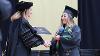 Acting President Dr. Shonna Riedlinger shakes hands with a graduate while handing her a degree.
