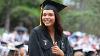 A graduate in her cap and gown smiles at the camera and gives a "thumbs up" sign as rain drops fall around her.